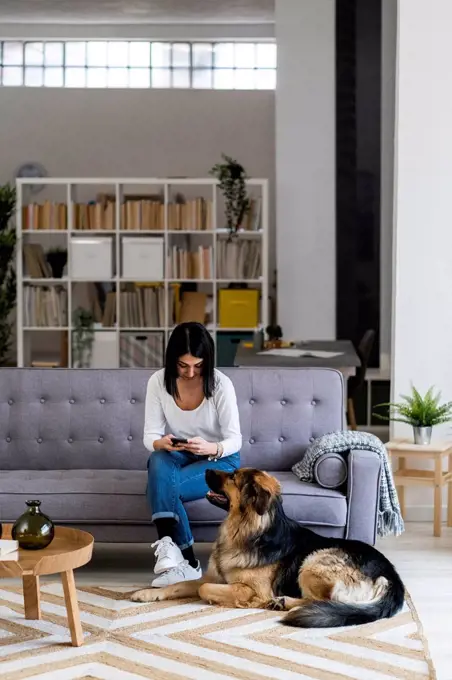 Young women using smart phone while sitting with dog in living room