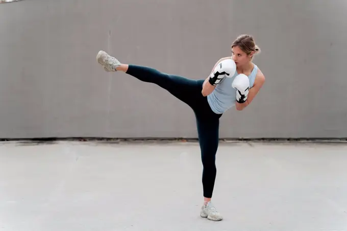 Woman with boxing glove practicing kickboxing against wall