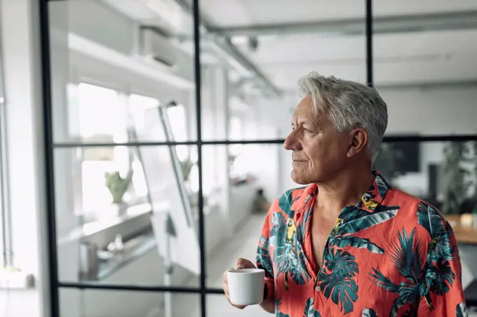 Businessman holding coffee cup while standing at office