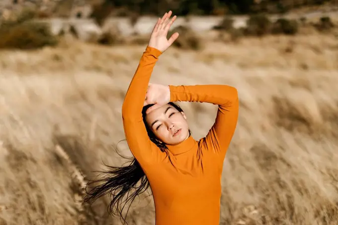 Beautiful woman with arms raised standing in field during windy day