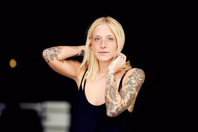 Tattooed woman with hand in hair standing at parking garage