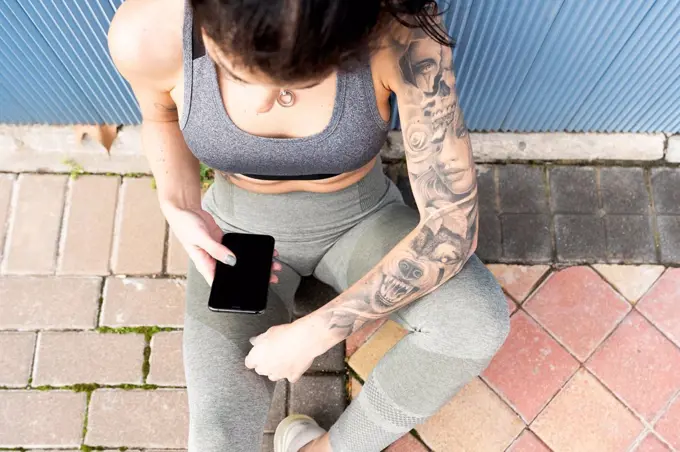 Mid adult woman using mobile phone while sitting on footpath