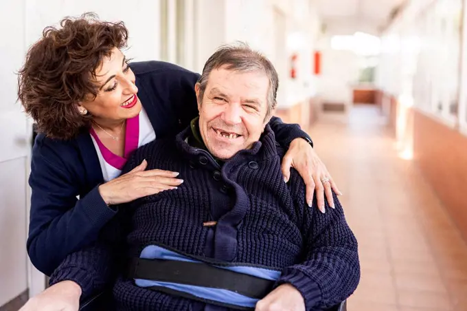 Happy nurse looking at disabled man in corridor of nursing home