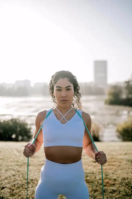 Female athlete with resistance band against clear sky at public park