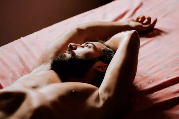 Young shirtless man resting in bedroom at home