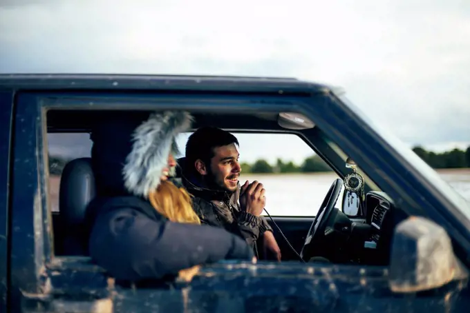 Young man using CB radio while traveling with female friend in car during winter