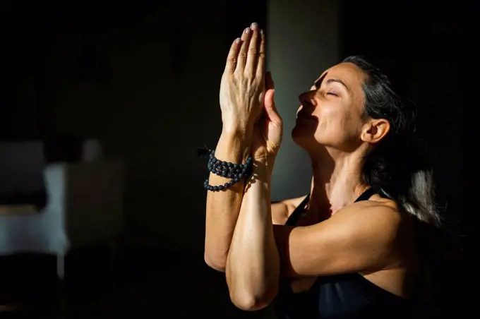 Yogini with eyes closed doing twisted arms meditation in living room in sunlight