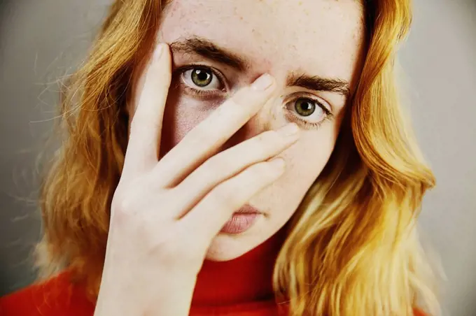 Blond teenage girl covering face with hand