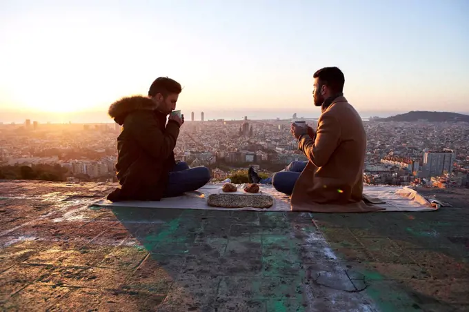 Gay couple having breakfast while sitting on observation point, Bunkers del Carmel, Barcelona, Spain