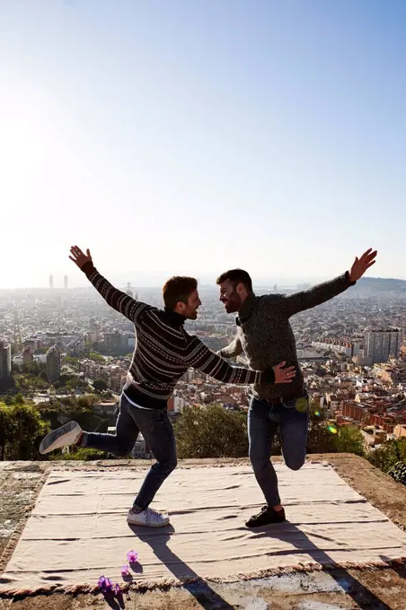 Cheerful gay couple with arms outstretched dancing on observation point, Bunkers del Carmel, Barcelona, Spain