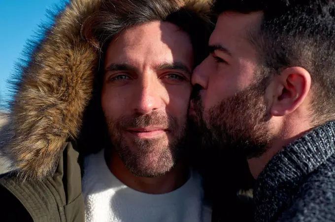 Close-up of man kissing on boyfriend's cheek wearing hood