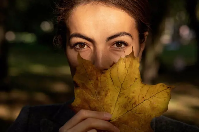 Businesswoman covering mouth with autumn leaf in park