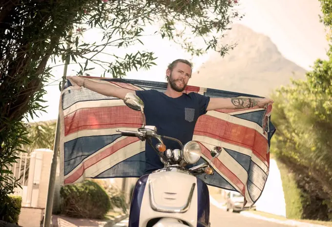 Man with arms outstretched holding national flag while sitting on motorcycle during summer