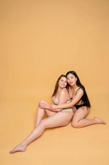 Smiling multi-ethnic female models in lingerie smiling posing against yellow background