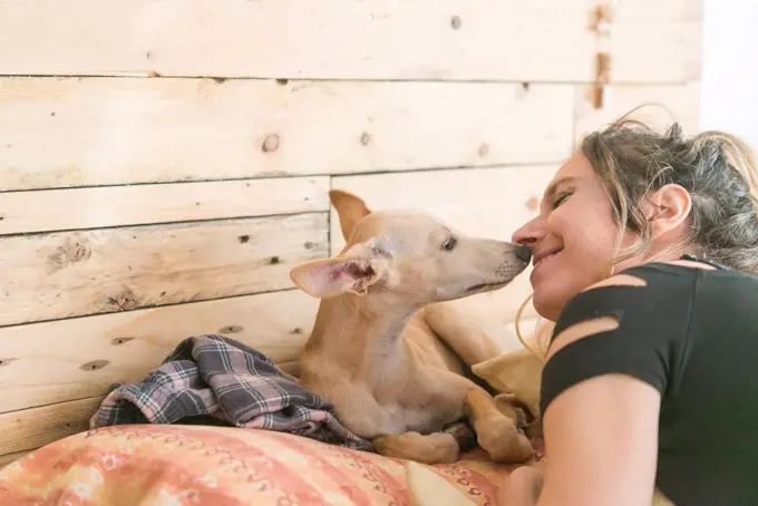 Smiling woman with Greyhound dog lying on bed