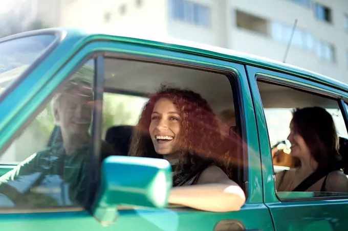 Smiling woman looking away while sitting with friends in car