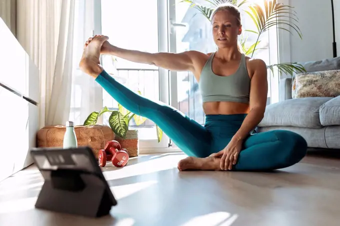 Young woman stretching leg while using digital tablet during workout at home