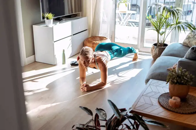 Woman practicing plank position while exercising on floor at home