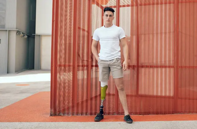 Confident disabled man with hand in pocket standing against orange wall