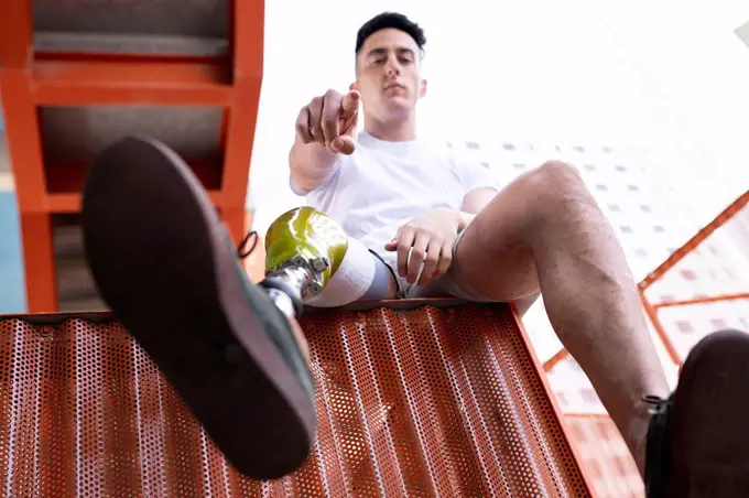 Amputated young man pointing while sitting on metal