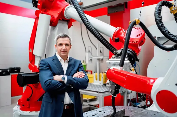 Male entrepreneur with arms crossed standing at robotics in factory