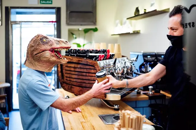 Man wearing dinosaur mask buying coffee from barista in cafe