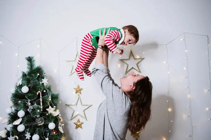 Smiling woman picking up baby boy while playing at home during Christmas