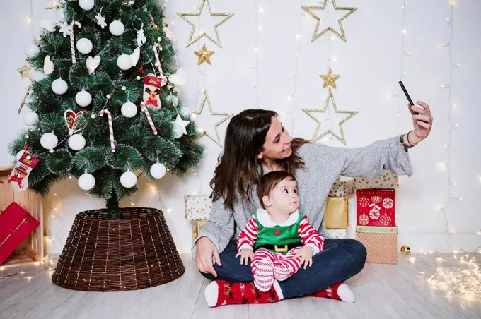 Mother taking selfie with son through mobile phone while sitting at home during Christmas