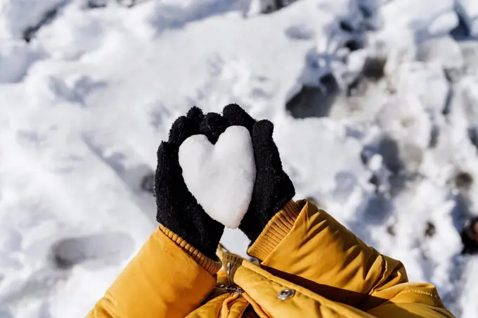 Girl's hands holding heart shaped snow in park