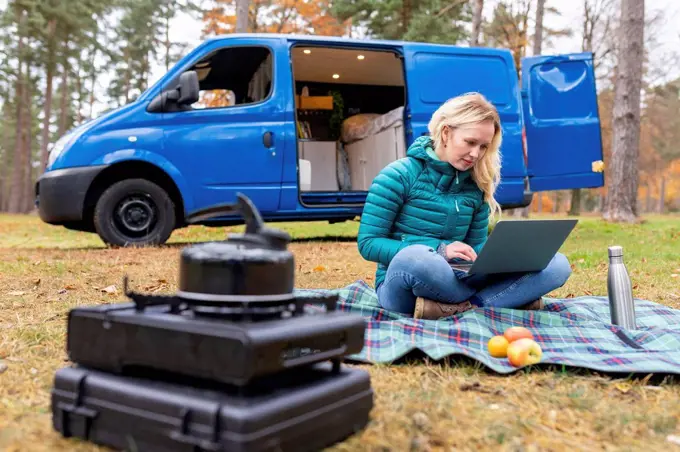 Woman working on laptop while sitting on picnic blanket at Cannock Chase