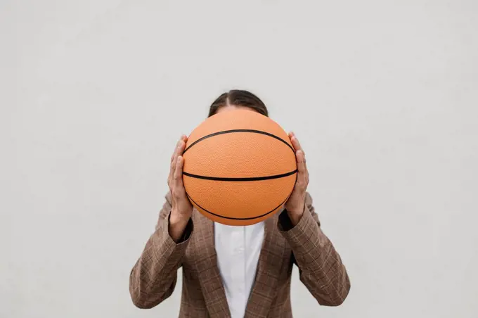 Female professional holding basketball in front of face against white wall