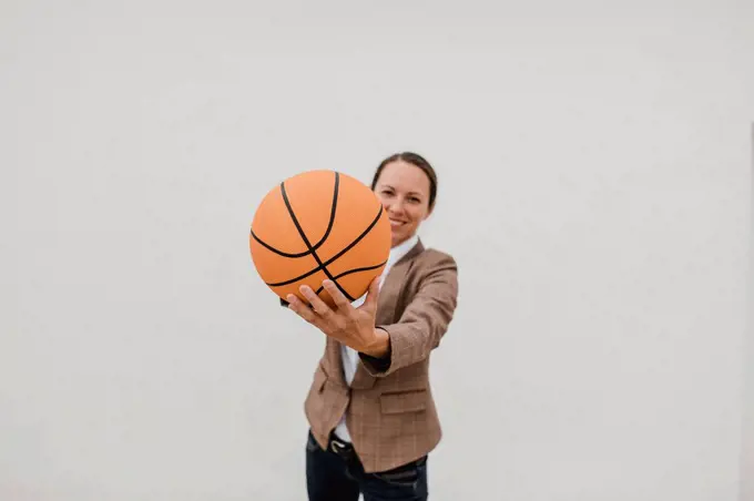 Playful female professional with basketball standing against white wall while taking break