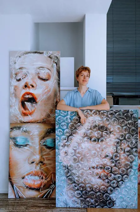 Smiling female artist standing with paintings in art studio