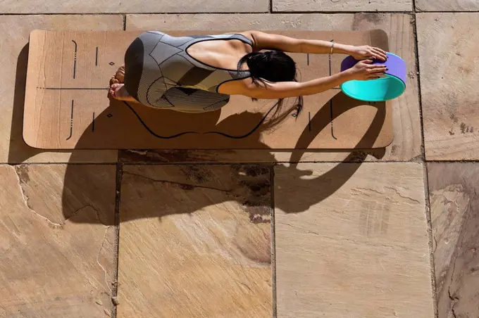 Female athlete practicing childs pose with yoga wheel on mat during sunny day