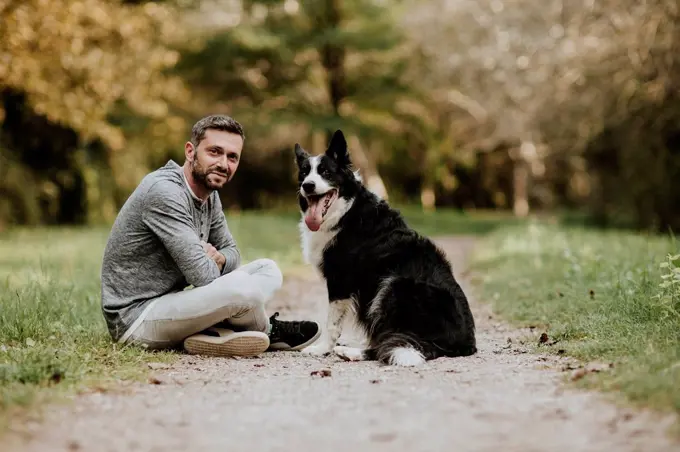 Smiling man and dog sitting on footpath at public park