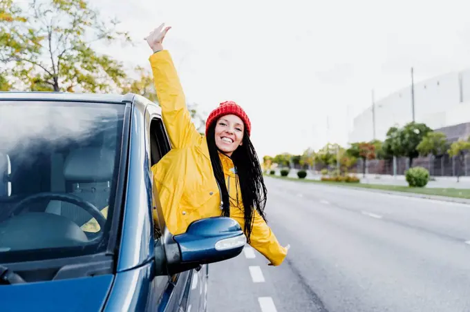 Carefree woman with arms outstretched leaning out of car