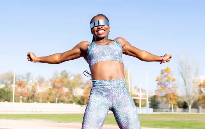 Cheerful female athlete in sunglasses jumping against clear sky on sunny day