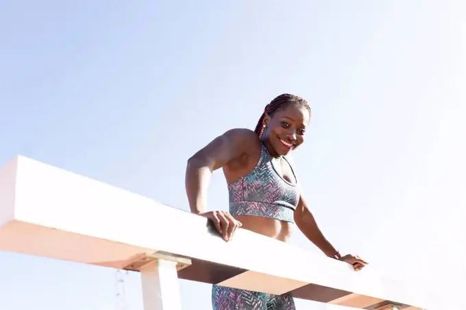 Happy sportswoman hanging on balance beam against clear sky during sunny day