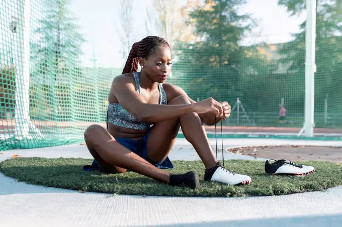 Female athlete tying shoelace against net in sports court