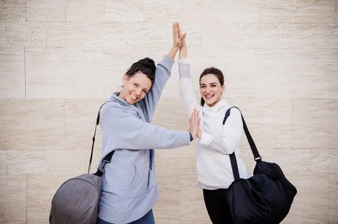 Smiling female sports people with hands clasped standing by wall