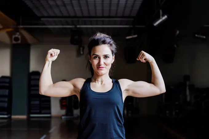 Beautiful female athlete flexing muscles in gym