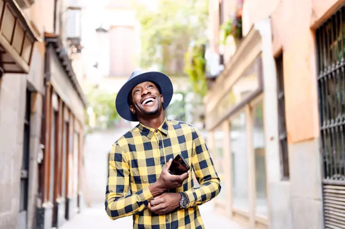 Smiling african man with smart phone looking away in city