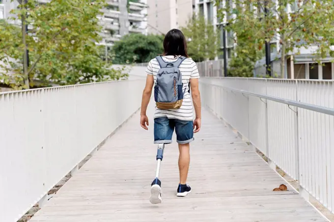 Amputed man with backpack walking on bridge in city