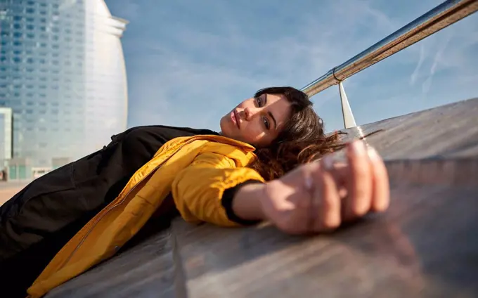 Carefree woman lying on retaining wall at pier during sunny day