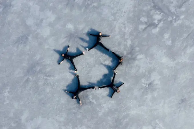 Aerial view of group of female ice-skaters lying together on surface of frozen lake