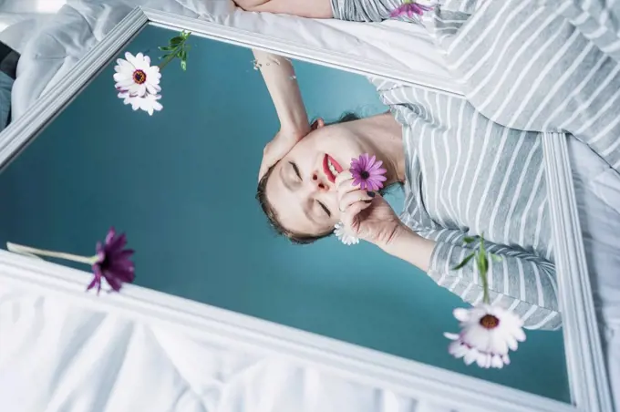 Young woman reflecting in mirror lying on bed