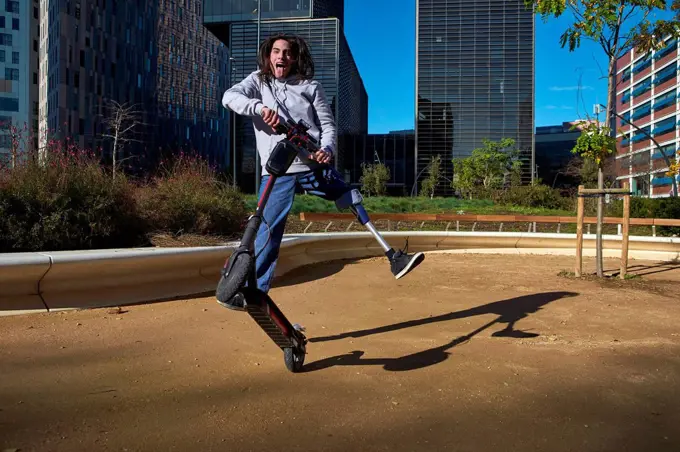 Playful disabled man practicing stunt on electric push scooter in playground against buildings in city