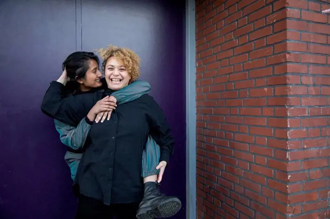 Young woman piggybacking girlfriend in front of building entrance