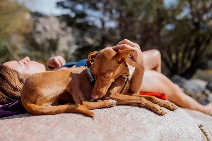 Woman relaxing while lying on rock with dog in forest at La Pedriza, Madrid, Spain