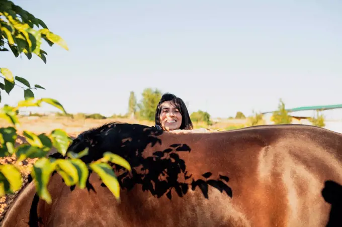 Smiling woman standing behind horse during sunny day